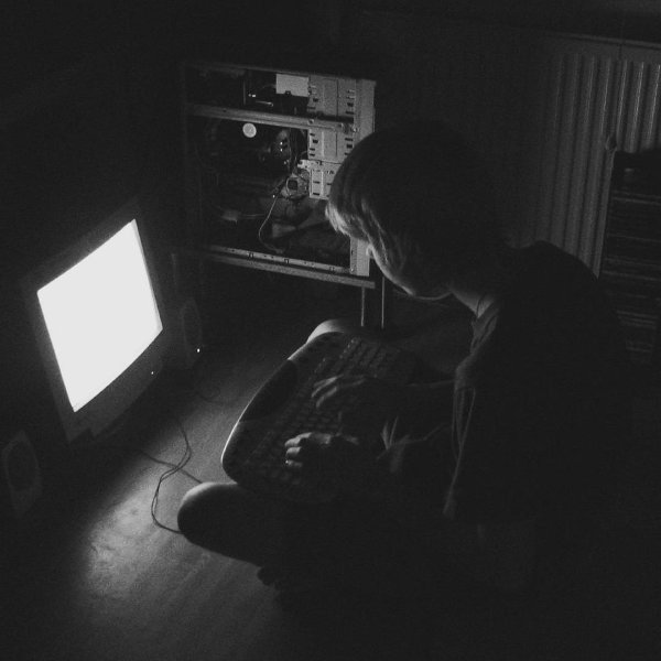 A teenager sitting in a dark room, only computer screen lighting it. Open PC case beside him.